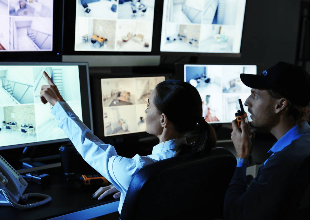 Two security guards analyze CCTV surveillance footage from a control room.